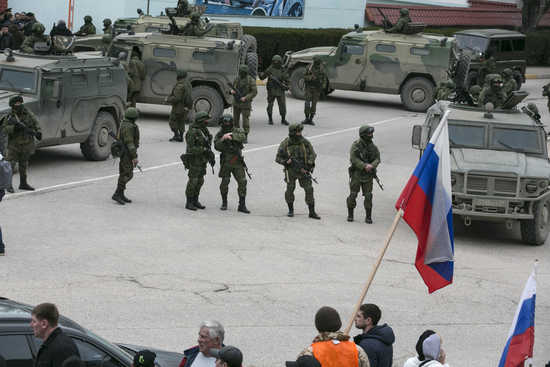 Pro-Russian men hold Russian flags in front of armed servicemen near Russian army vehicles outside a Ukrainian border guard post in the Crimean town of Balaclava March 1, 2014. Ukraine accused Russia on Saturday of sending thousands of extra troops to Crimea and placed its military in the area on high alert as the Black Sea peninsula appeared to slip beyond Kiev's control. REUTERS/Baz Ratner (UKRAINE - Tags: MILITARY POLITICS CIVIL UNREST) - RTR3FVDV